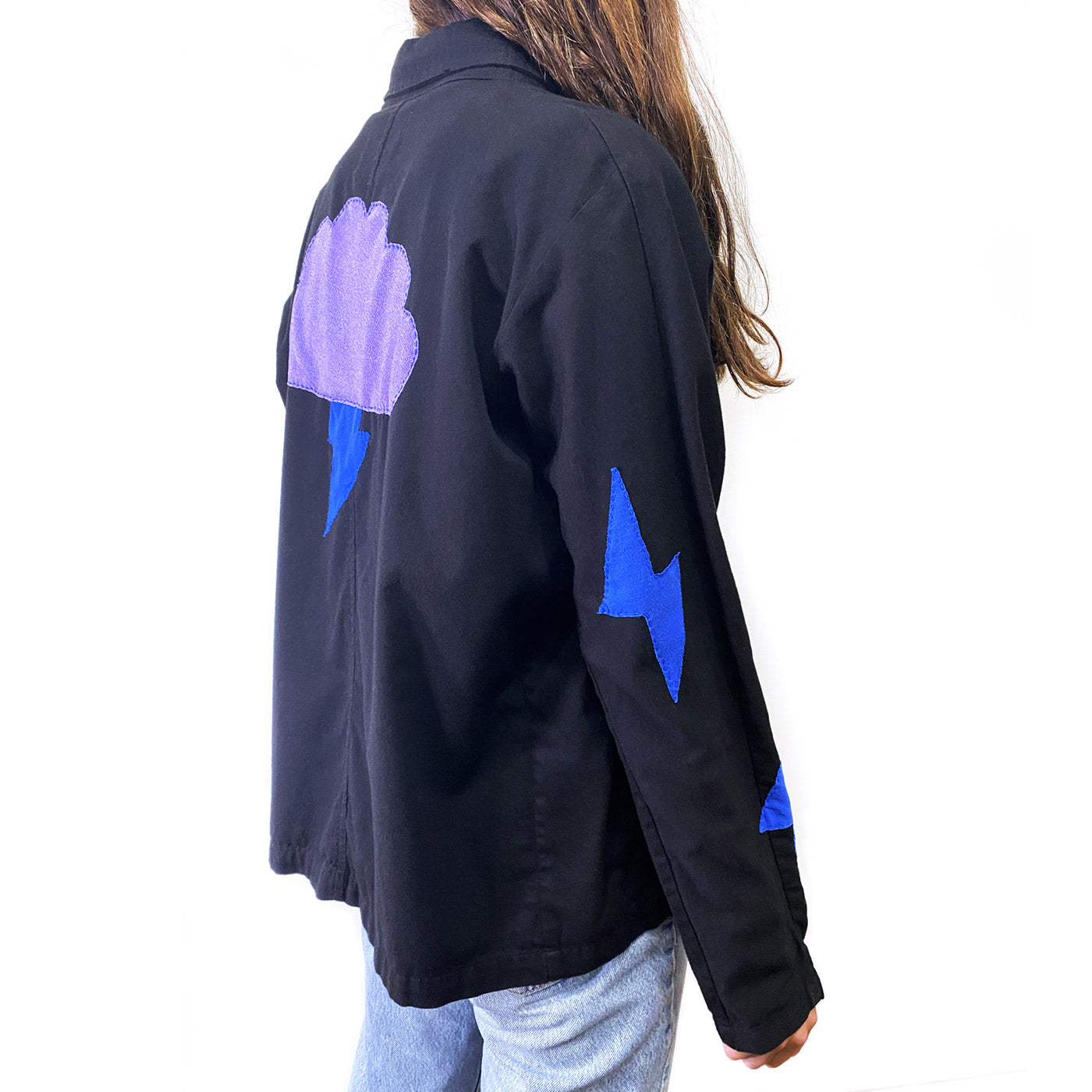 Side view of person with long brown hair wearing black jacket with handsewn designs in light purple and blue