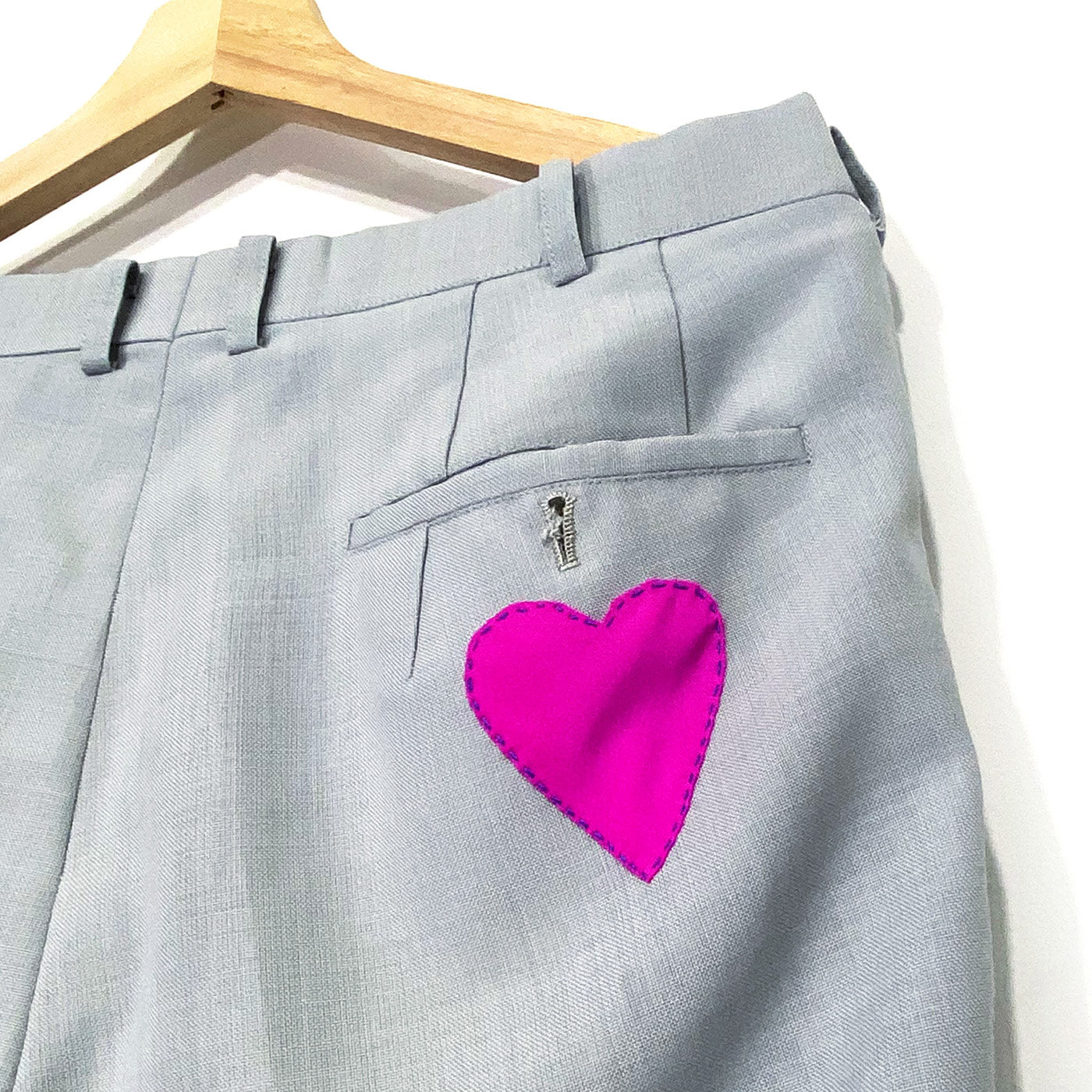The back of grey trousers with a pink heart hand stitched on the pocket