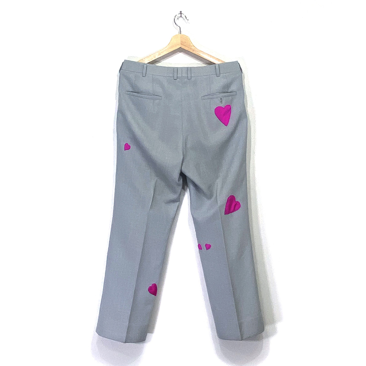 The back side of light grey trousers with several differently sized pink hearts sewn on