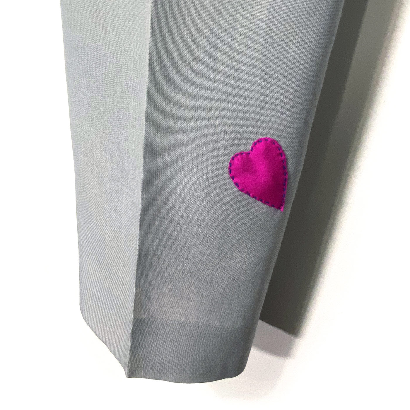 The bottom of one leg of grey trousers with a small pink heart sewn on one side