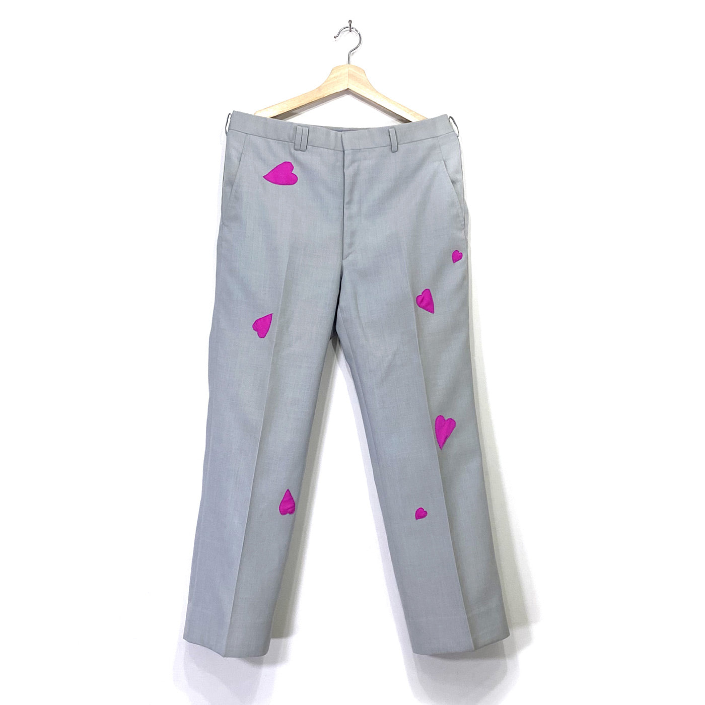 The front of grey dress pants with seven intense pink hearts sewn in various locations