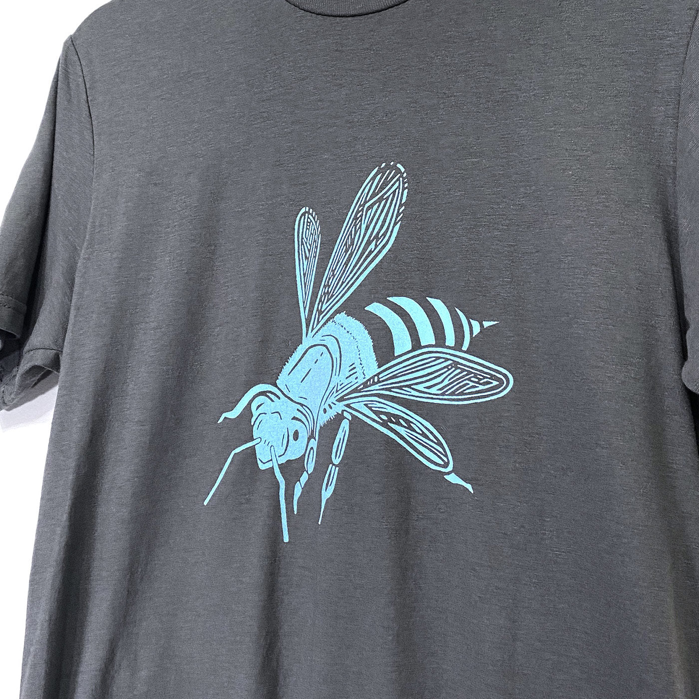 Close up of grey t-shirt with an illustration of a bee in light blue printed on the front