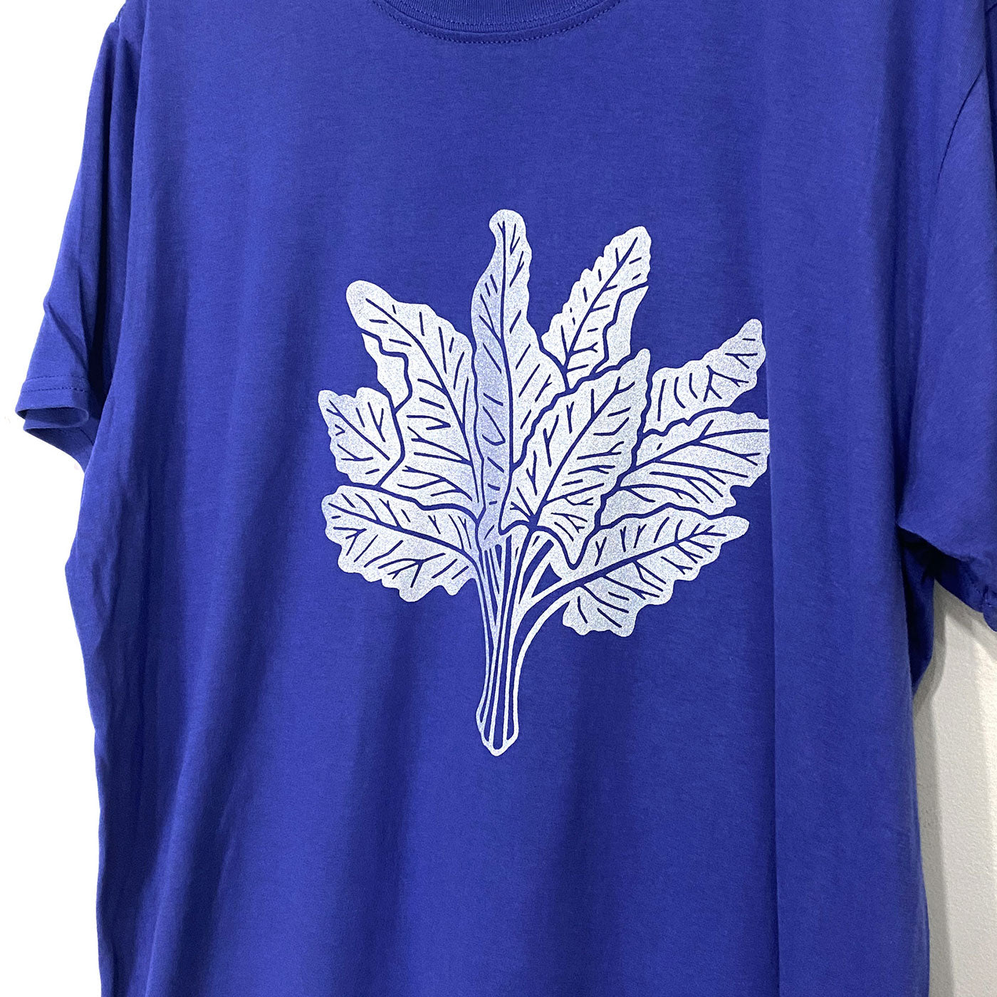 Detail of a silver chard drawing screen printed on the front of a blue short sleeveshirt